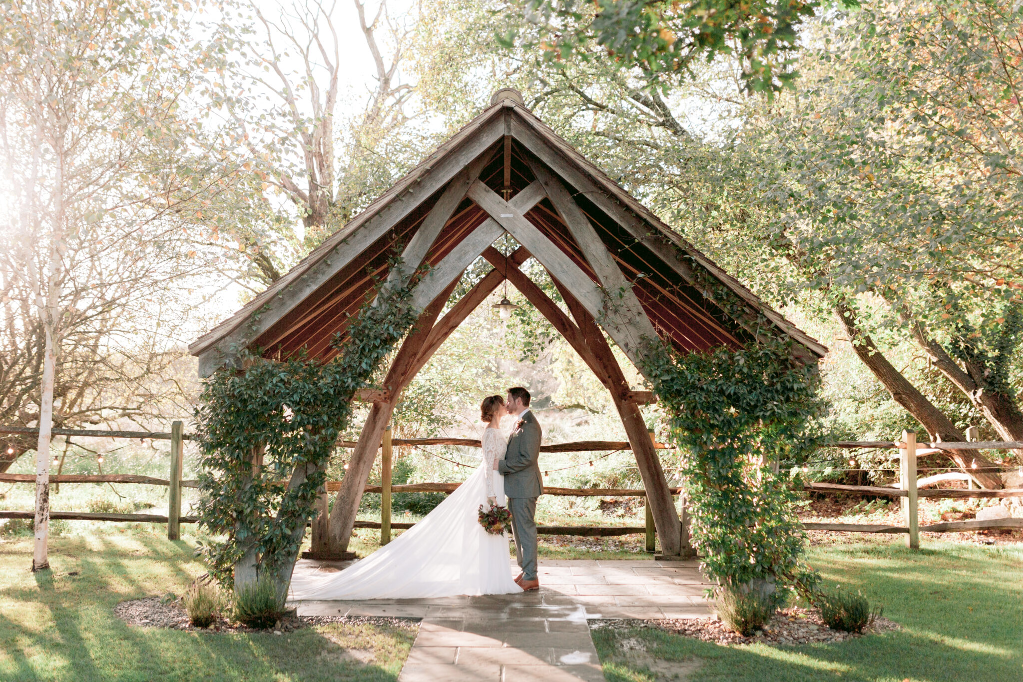 Couple share a kiss under the arbour at their autumnal wedding at Millbridge Court in Surrey.