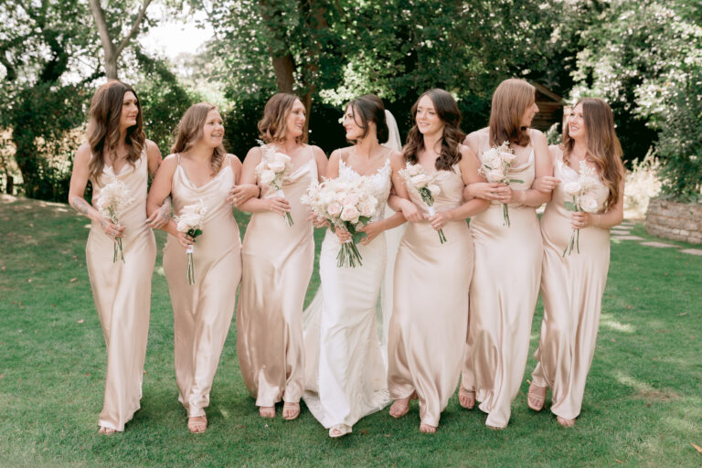 Elegant Bride with her six bridesmaids holding their bouquets of blush pink roses in the garden of Millbridge Court, Surrey.