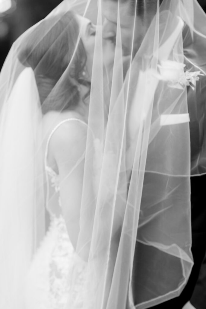 Couple share a kiss underneath the Bride's veil at their black tie wedding at Millbridge Court in Surrey.